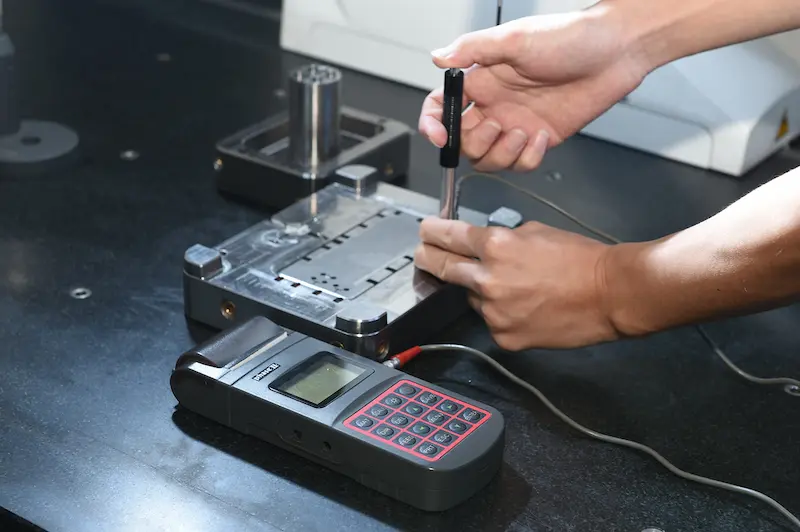 Technician performing precision inspection on plastic part using a CMM measuring machine.